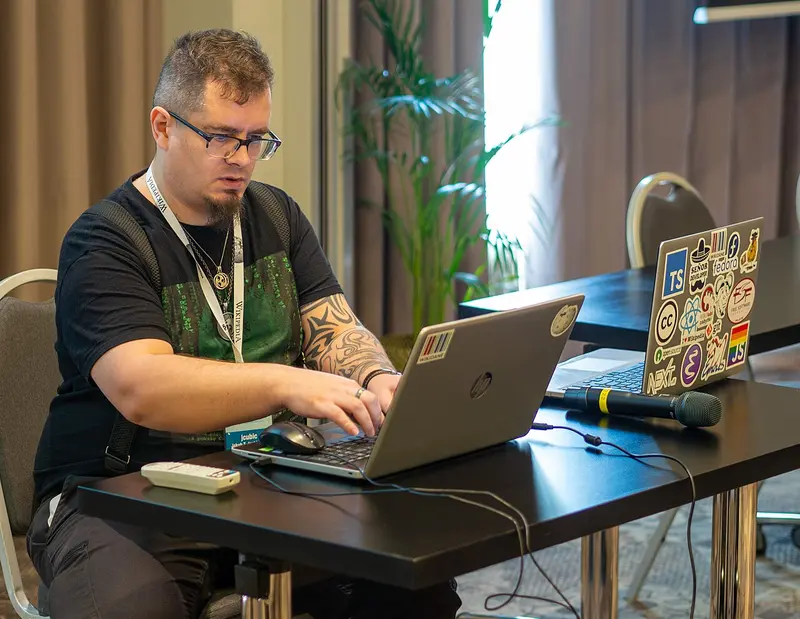 Jakub T. Jankiewicz podczas prezentacji, siedzący za laptopem w koszulce WikiTrenera z widocznym tatuażem na ramieniu
